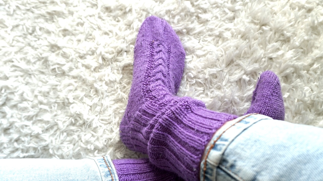 Feet wearing knitted socks featuring cable knit pattern in purple yarn