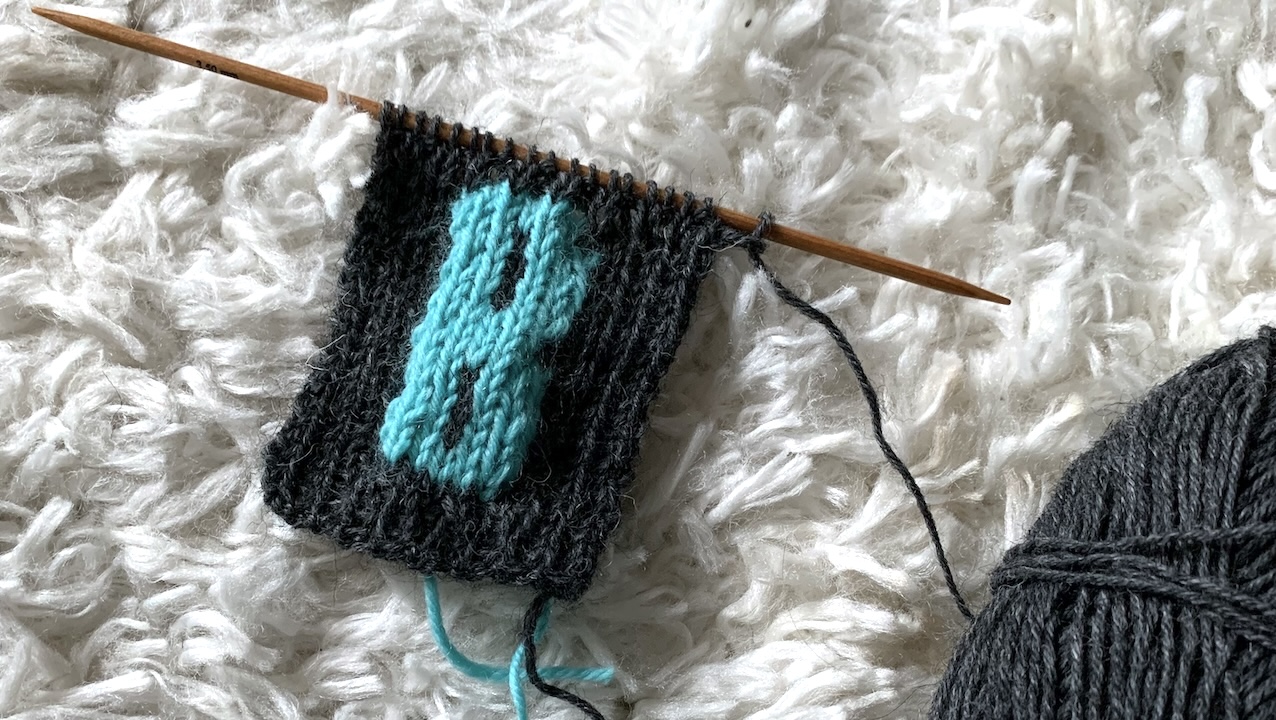 Dark gray knitted fabric with a knitted turquoise letter B