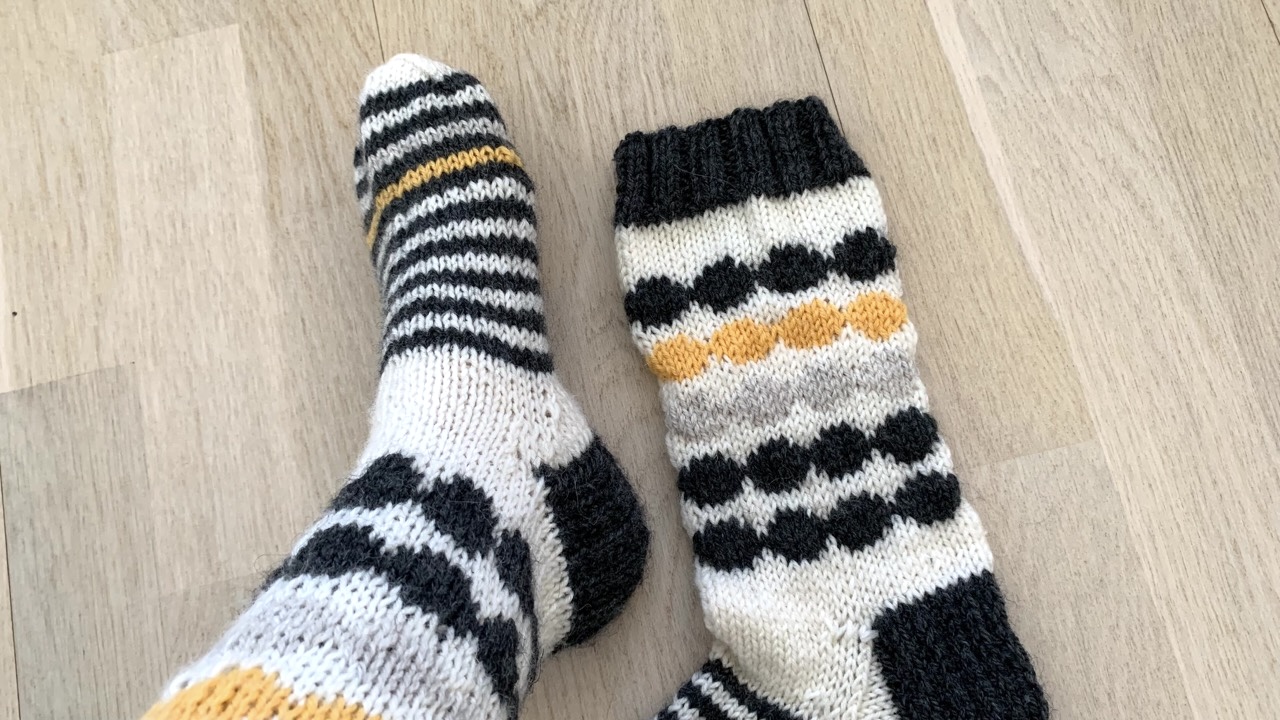 Knitted socks featuring circle colorwork patterns and stripes in white, light gray, dark gray, and yellow yarn