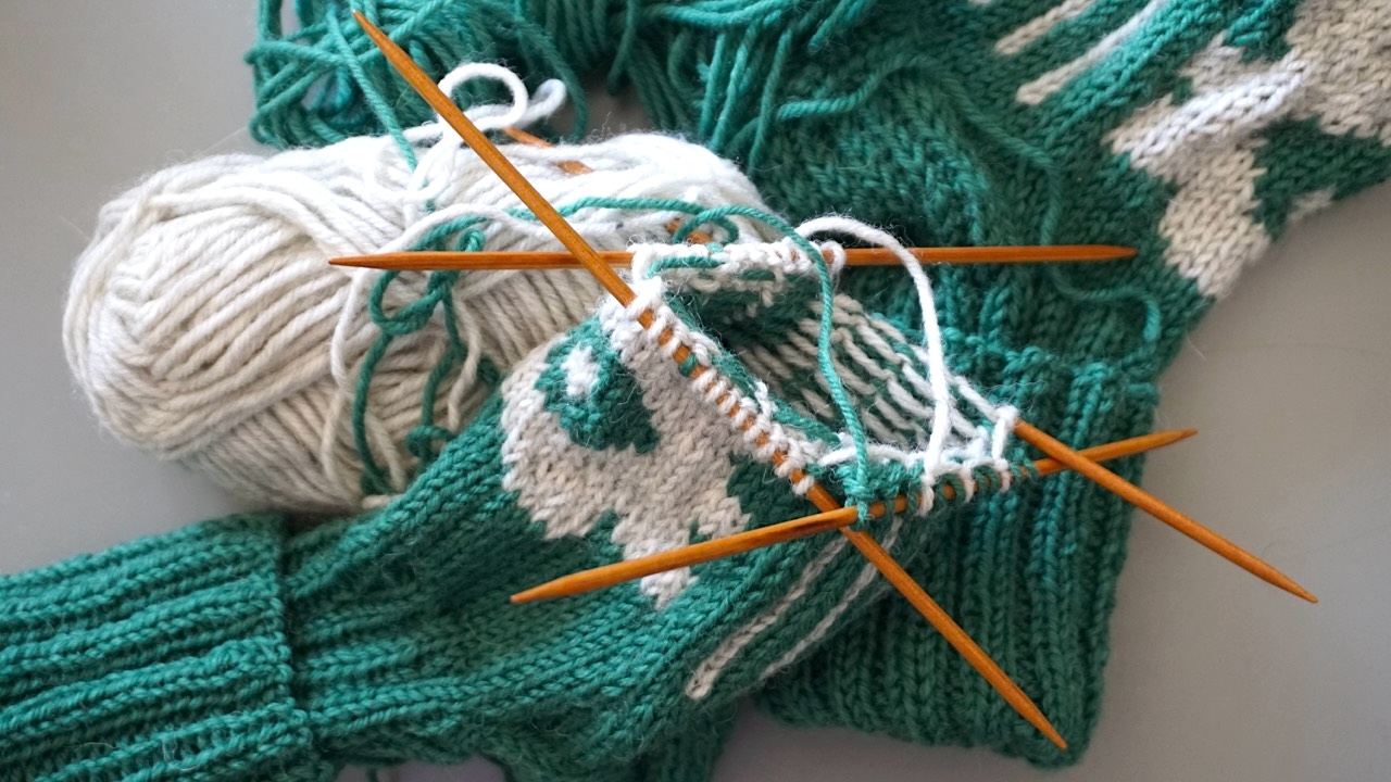 Unfinished colorwork knitting project on double pointed needles next to balls of yarn