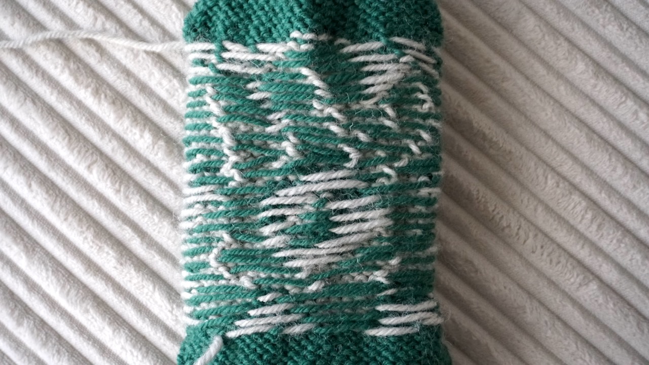 Close-up of a green and light gray colorwork knitting pattern showing the wrong side with floats