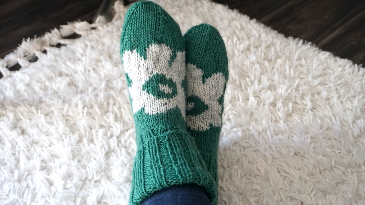 Feet wearing dark green knit socks featuring light gray colorwork flower pattern