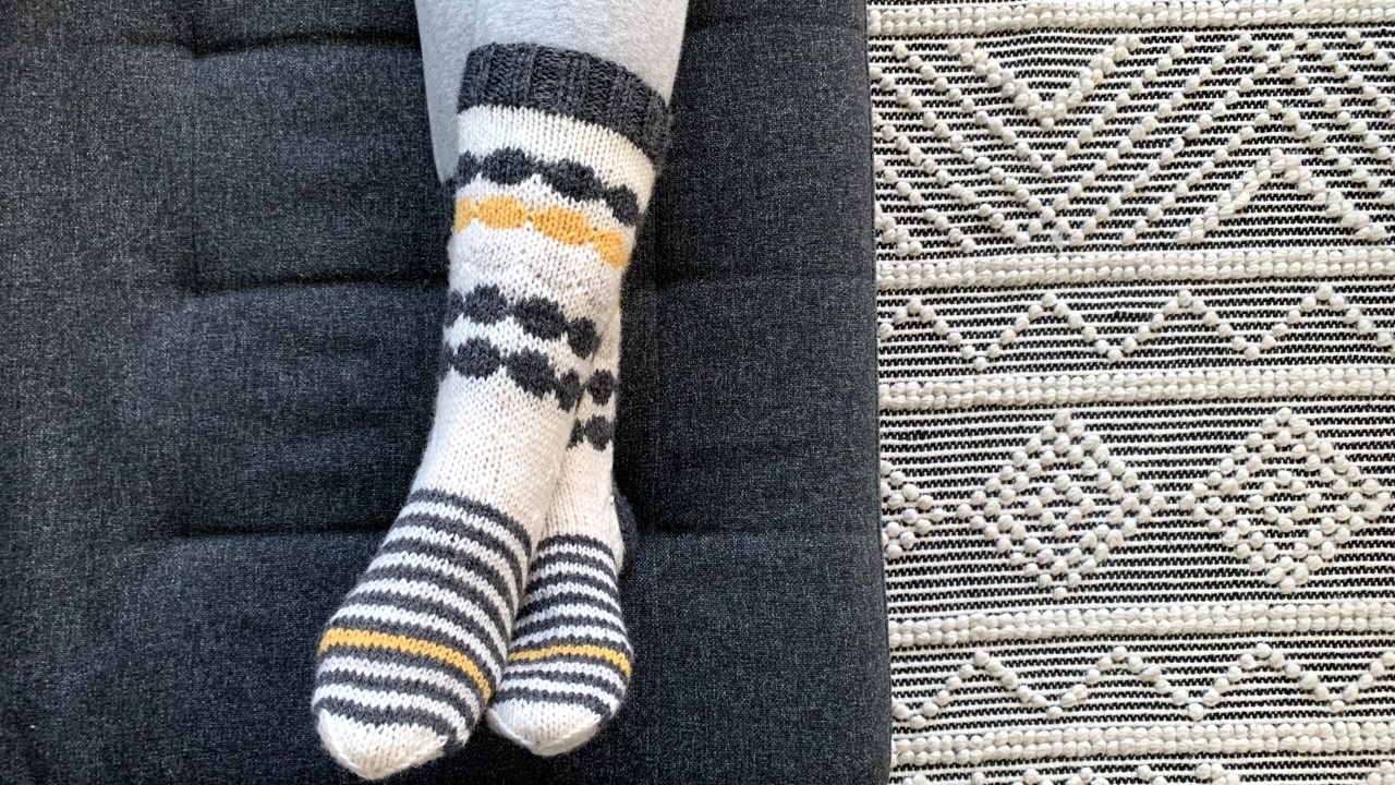 Feet wearing knit socks featuring circle colorwork patterns and stripes in different colors of yarn