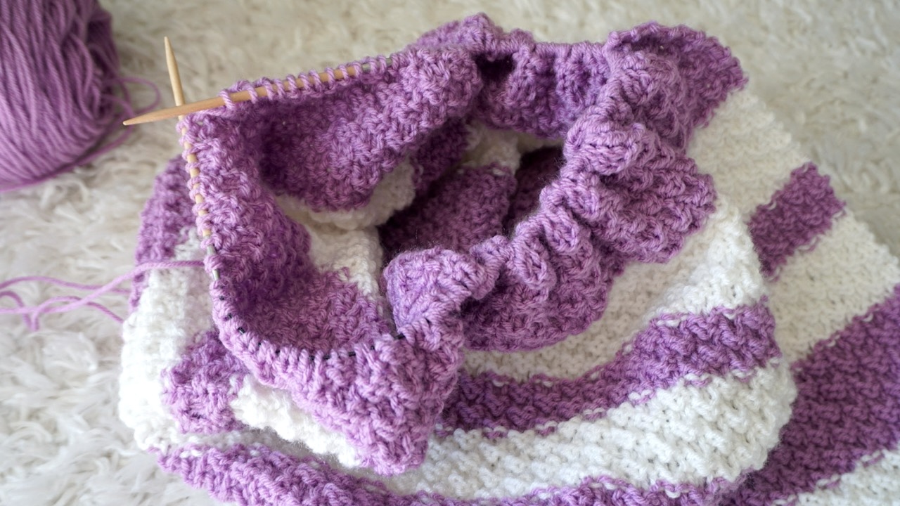 An unfinished knitting project with purple and white stripes on wooden circular needles