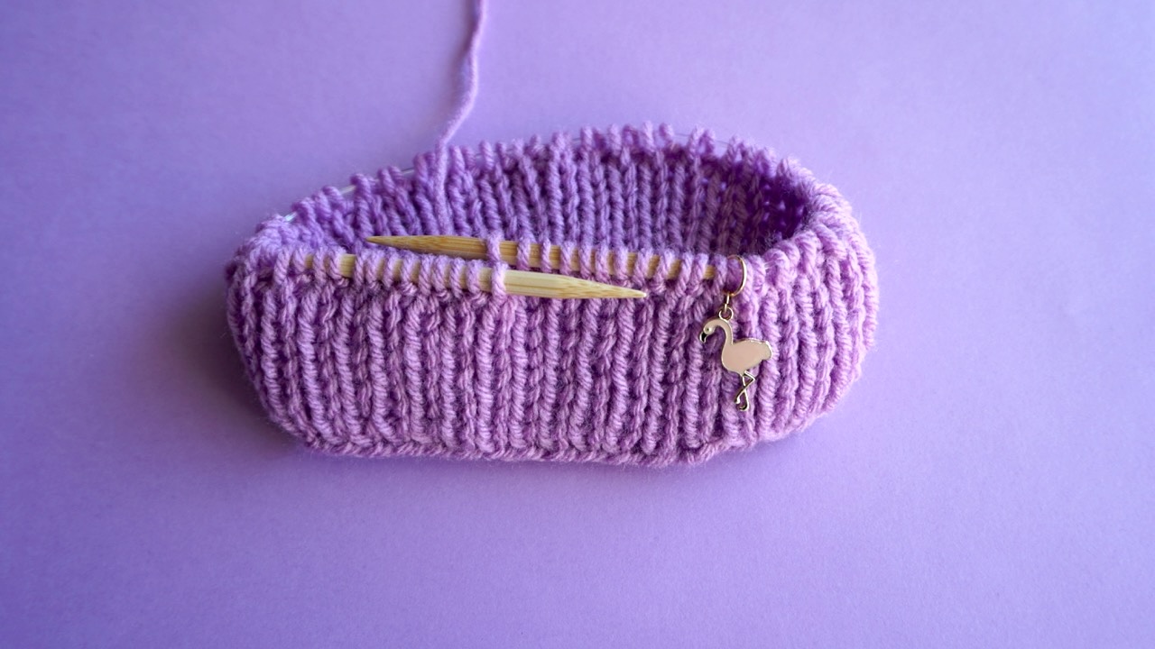 A purple knitting project and a flamingo shaped stitch marker on wooden circular needles