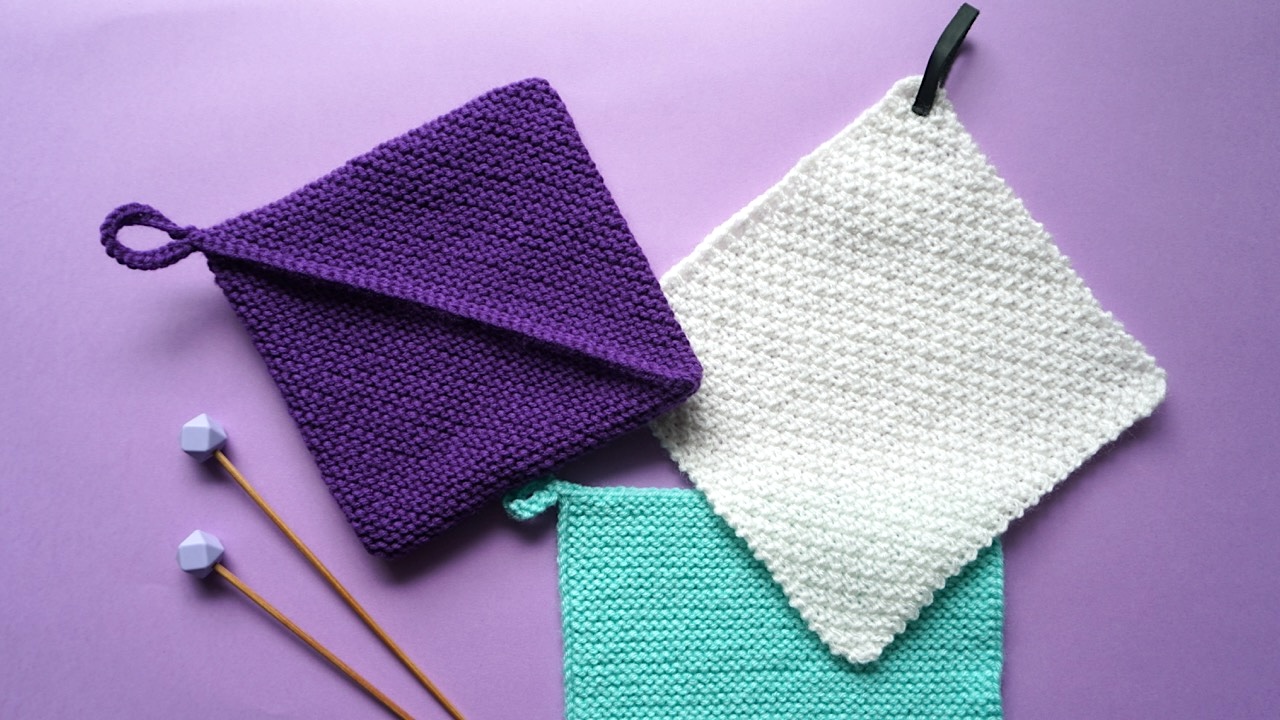 Purple, white, and turquoise knitted potholders next to a pair of knitting needles