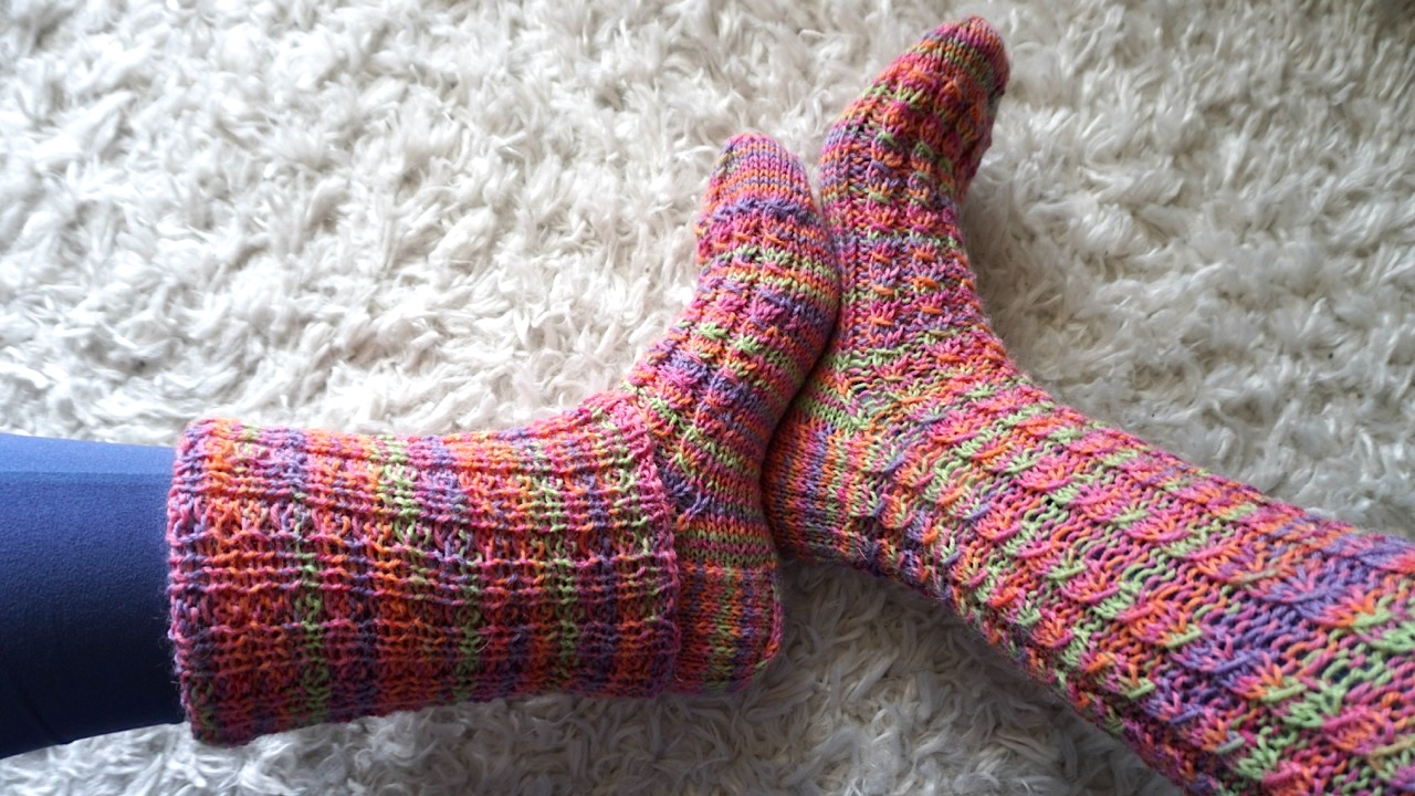 Feet wearing knitted socks featuring mock cable stitch in bright, colorful yarn