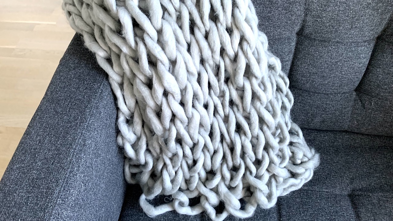 Hand knit blanket in light gray yarn laying on a dark gray sofa