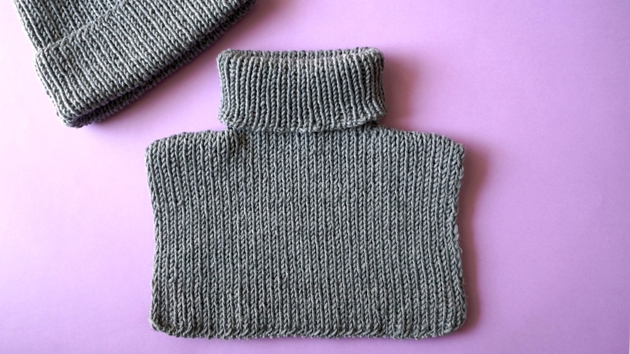 Knitted neck warmer featuring rib stitch in gray yarn next to a gray beanie