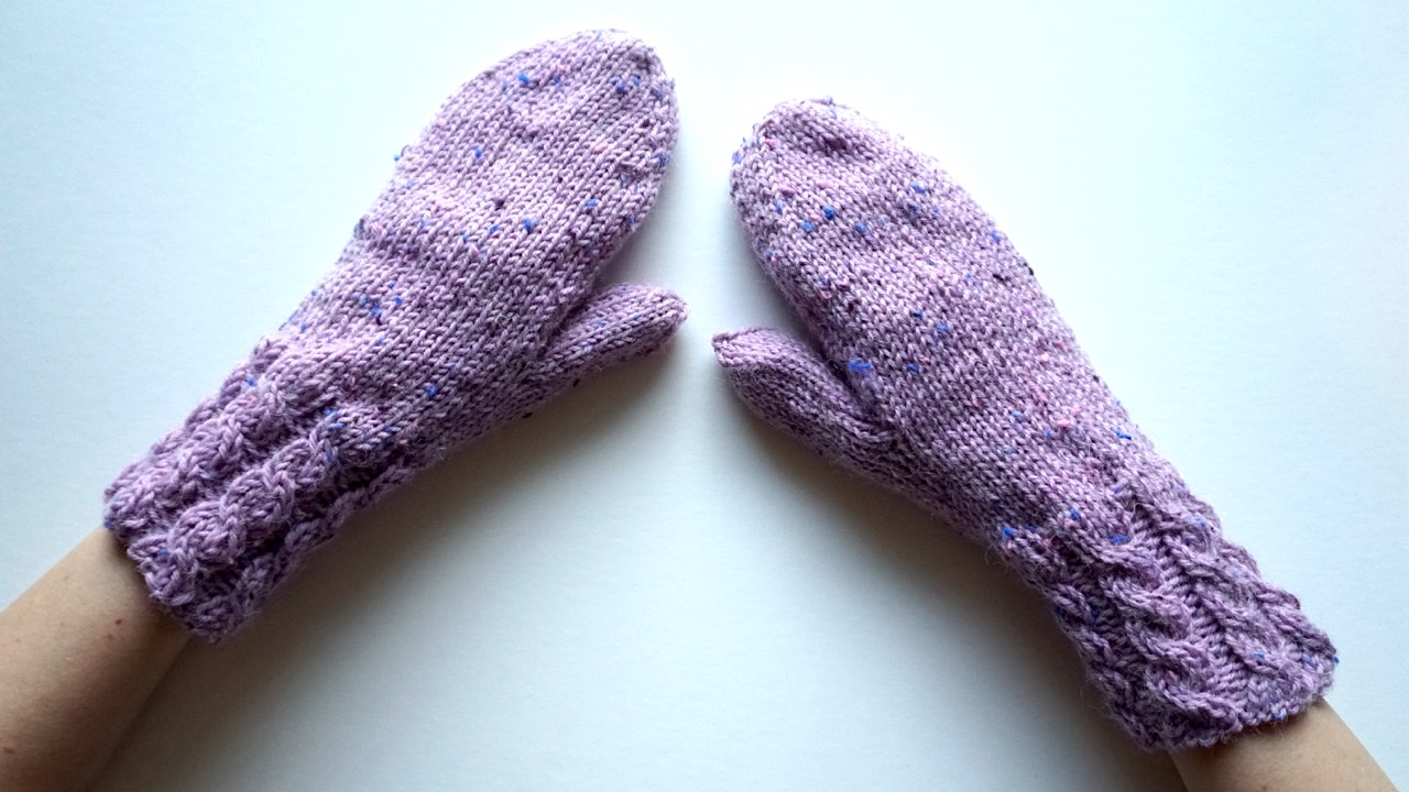 Hands wearing knitted mittens featuring cables in light purple yarn