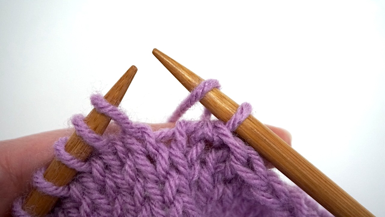 Wrapping purple yarn over the right needle in an unfinished knitted piece