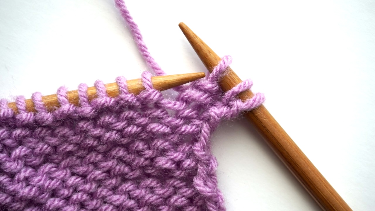 An unfinished knitting project with three purl stitches on the right-hand needle