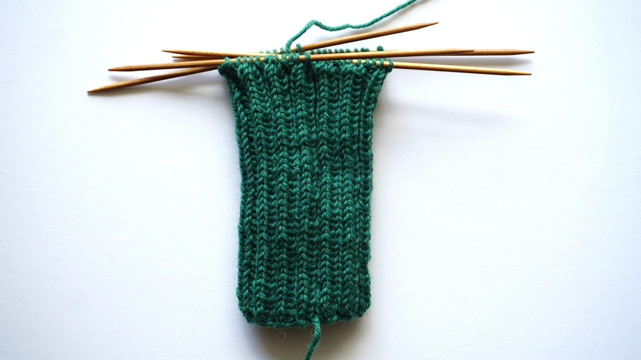 Step-by-step knitting photo showing the sock cuff in dark green yarn