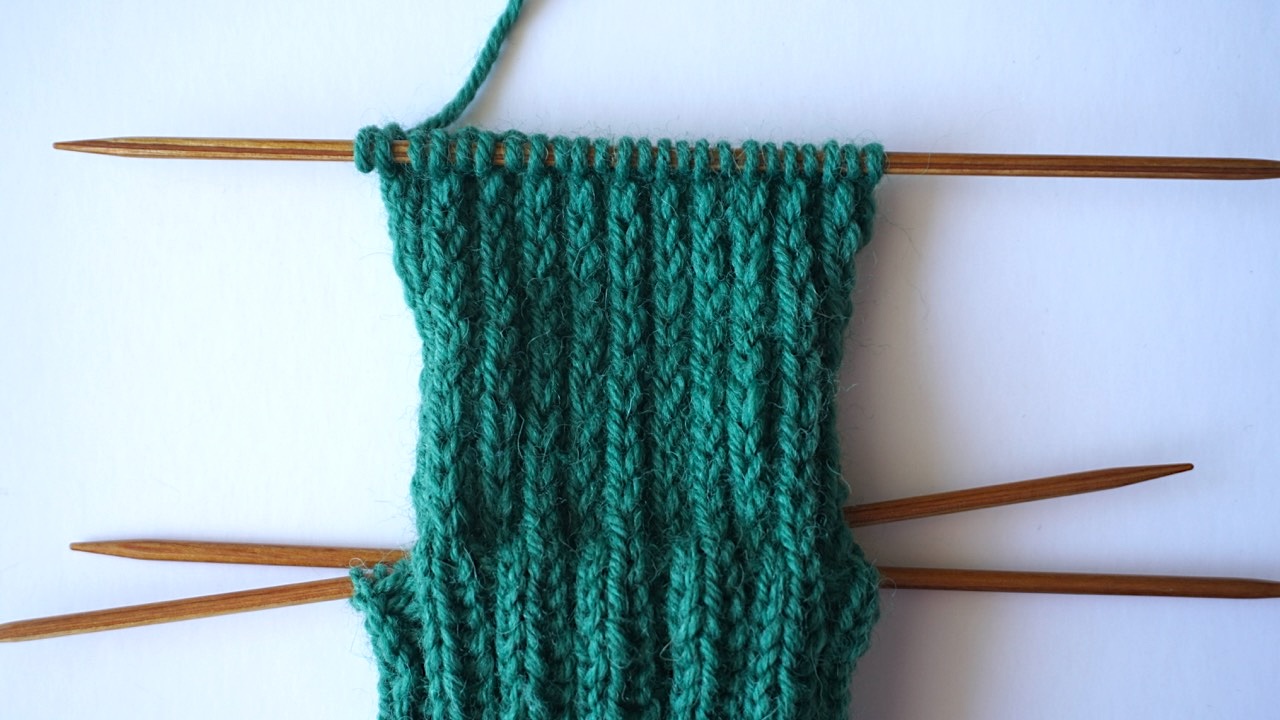 Step-by-step knitting photo showing the reinforced heel flap in dark green yarn