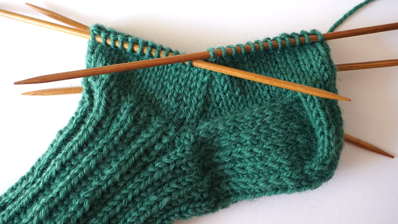 Step-by-step knitting photo showing the gusset decreases of a dark green knitted socks