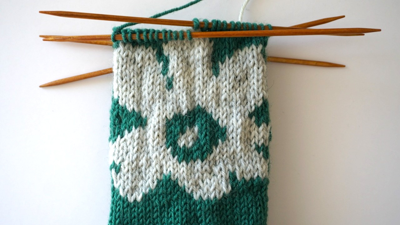 Close-up photo of knitting colorwork socks pattern in light gray yarn