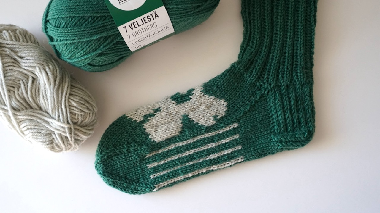Dark green knitted socks featuring unikko colorwork pattern and stripes in light gray yarn