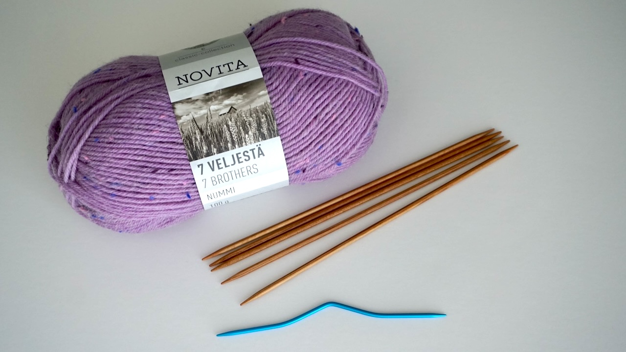 Skein of purple yarn, five double pointed needles and cable needles laying next to each other