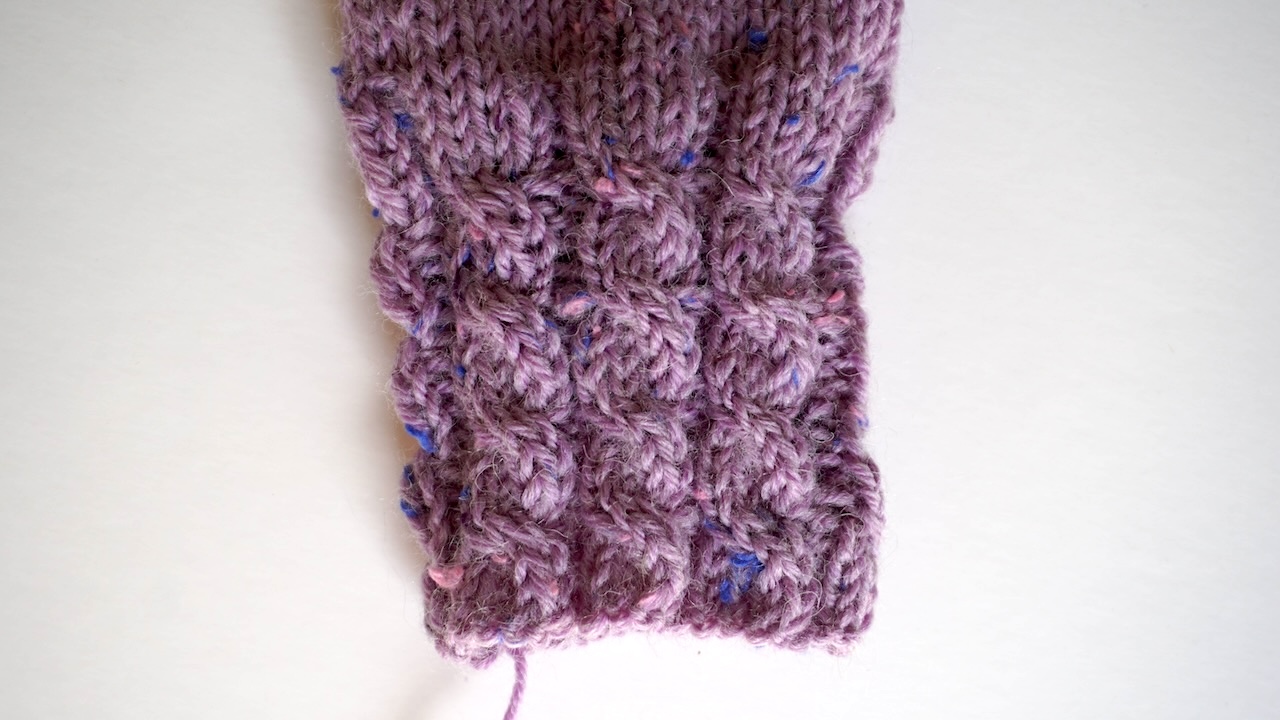 Step-by-step knitting photo showing finished mitten cuff in cable stitch pattern