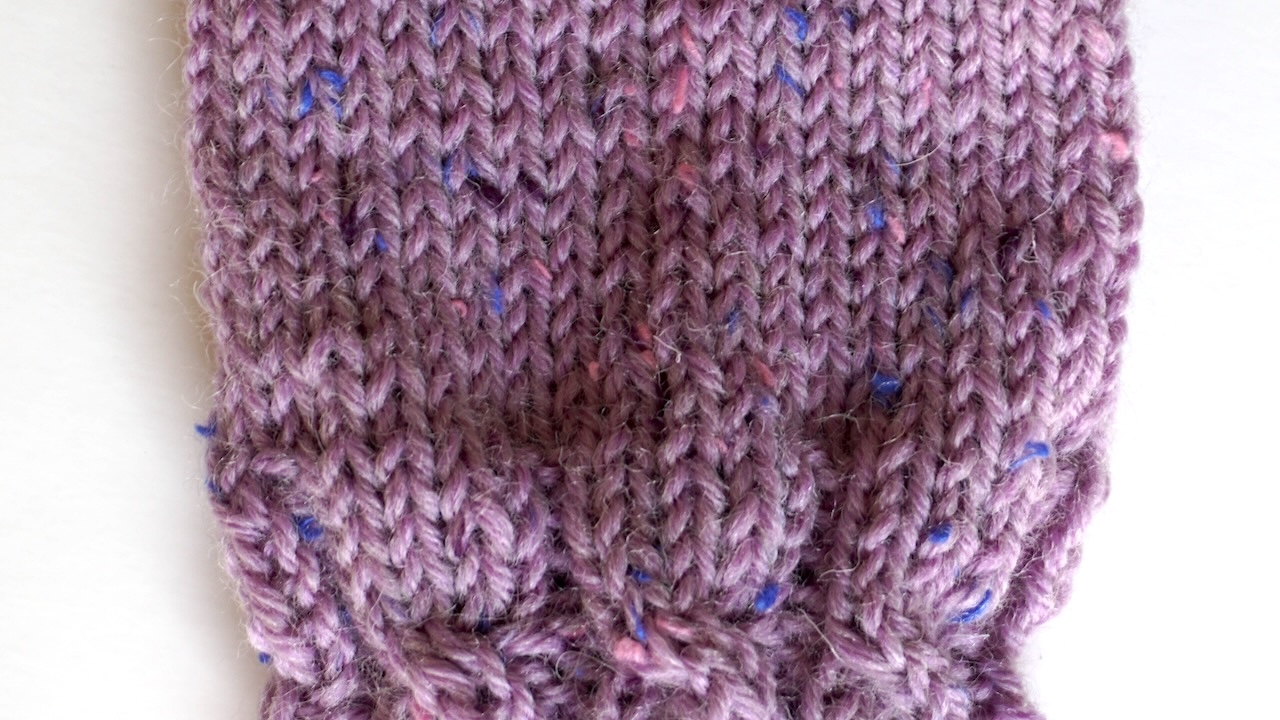 Step-by-step knitting photo showing the lower half of the hand section featuring stockinette stitch in purple yarn