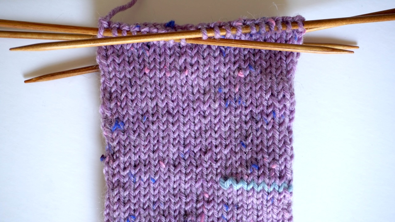Step-by-step knitting photo showing the upper half of the hand section featuring stockinette stitch in purple yarn