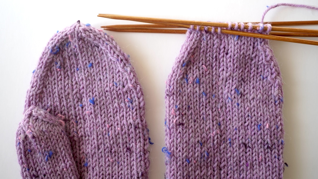 Close-up knitting photo of a finished mitten top next to an unfinished mitten top