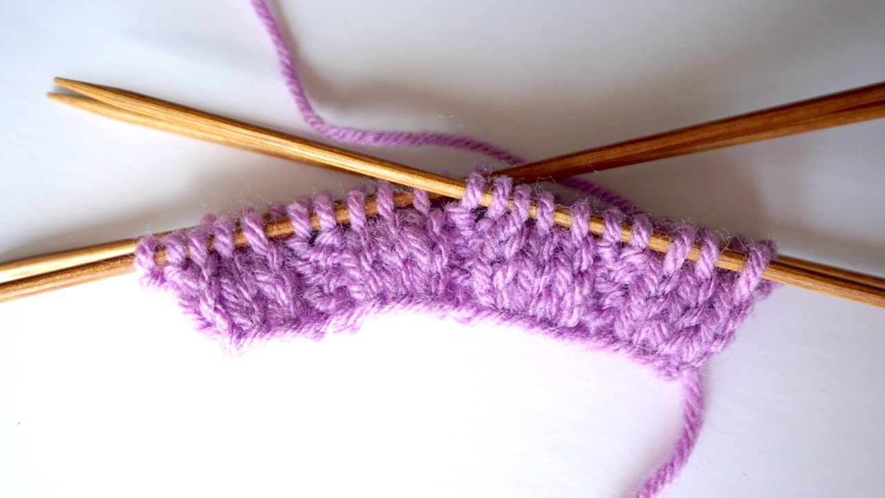 Step-by-step knitting photo showing needles with the initial ribbing setup for mock cable knit stitch