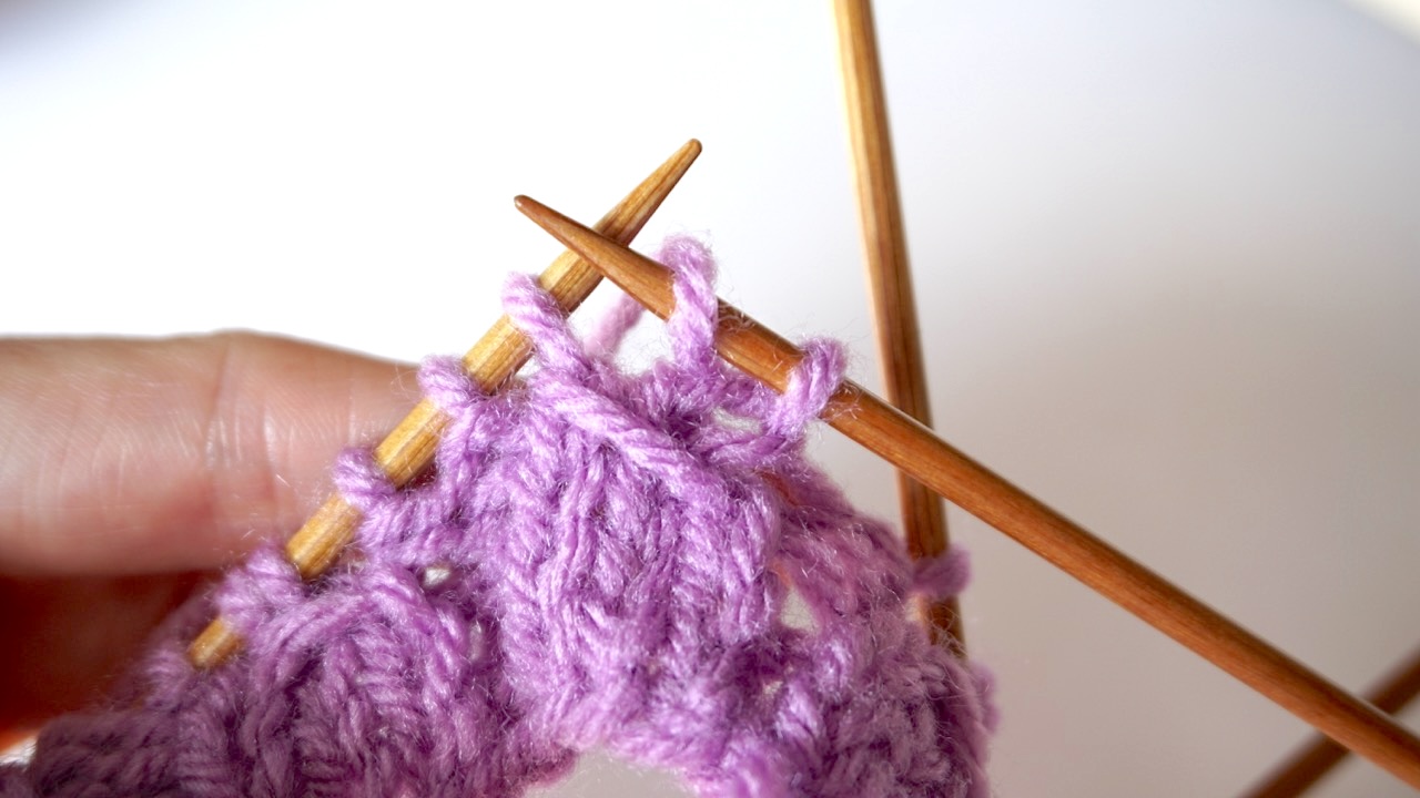 Step-by-step knitting photo showing hands wrapping the yarn with the right needle for mock cable knit stitch