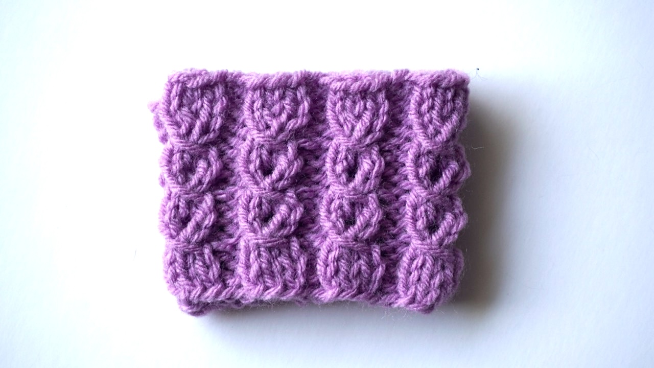 Close-up photo of mock cable stitch pattern in purple yarn showing cable-like texture