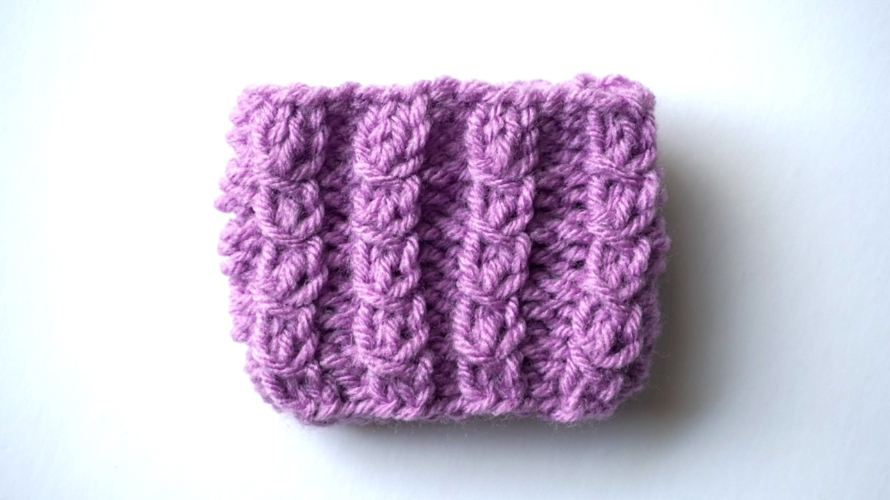 A purple knitting swatch in simple 3-stitch mock cable
