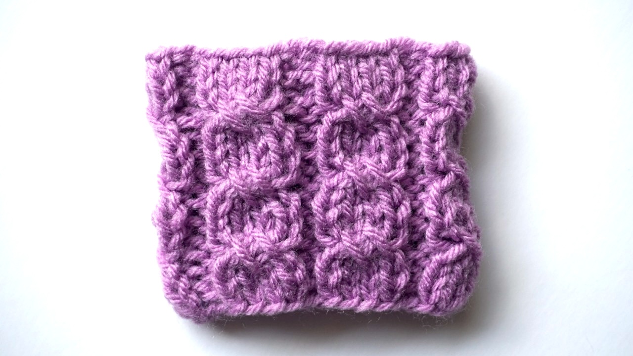 A purple knitting swatch in cross stitch mock cable pattern