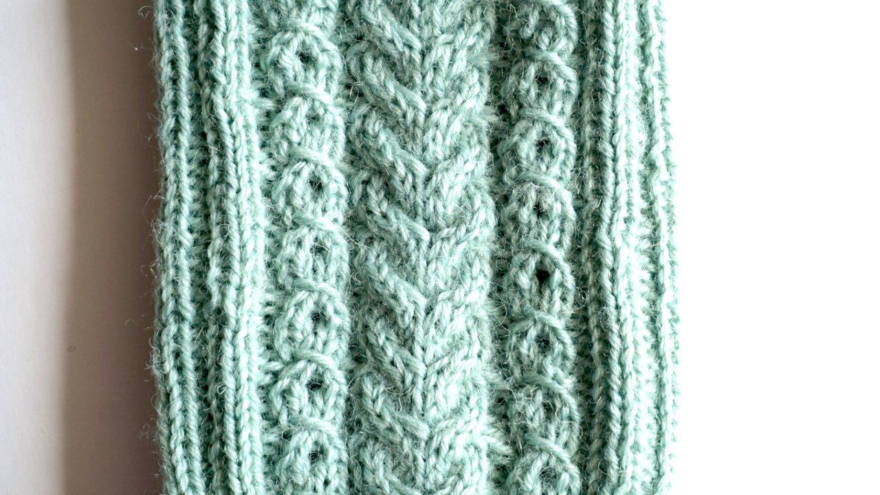 Close-up photo of mock cable knit stitch texture in light green yarn next to a real cable stitch