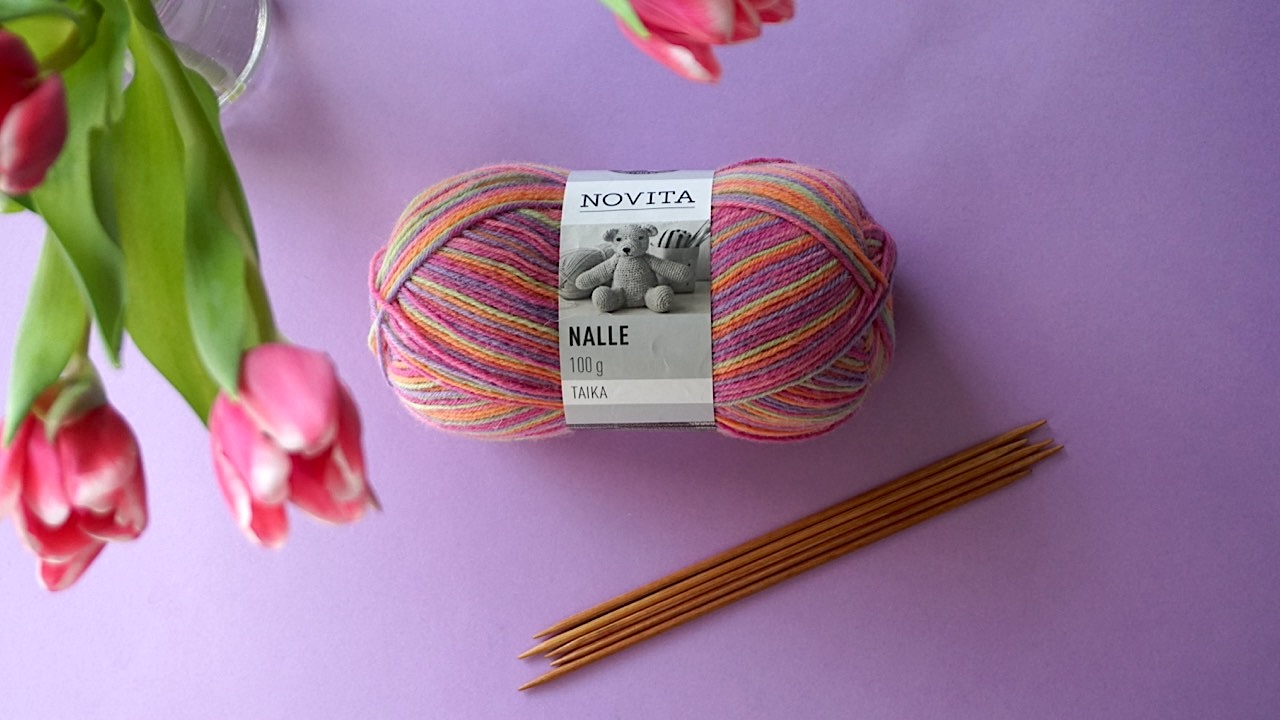 A colorful skein of yarn next to double pointed needles and pink tulips