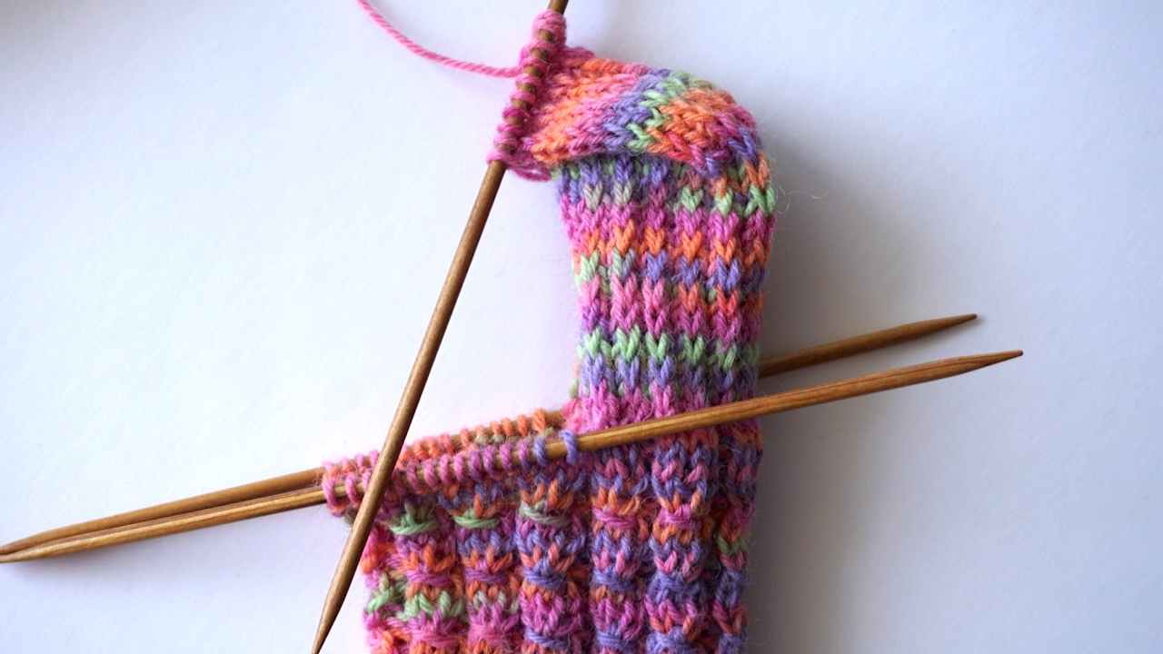Step-by-step knitting photo showing the mock cable sock heel in colorful yarn