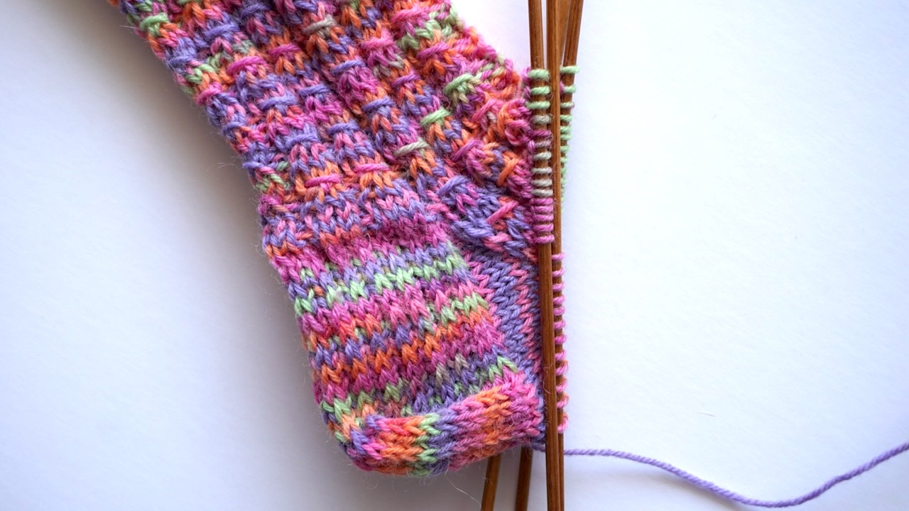 Step-by-step knitting photo showing the gusset decreases and the mock cable pattern in the cuff and foot
