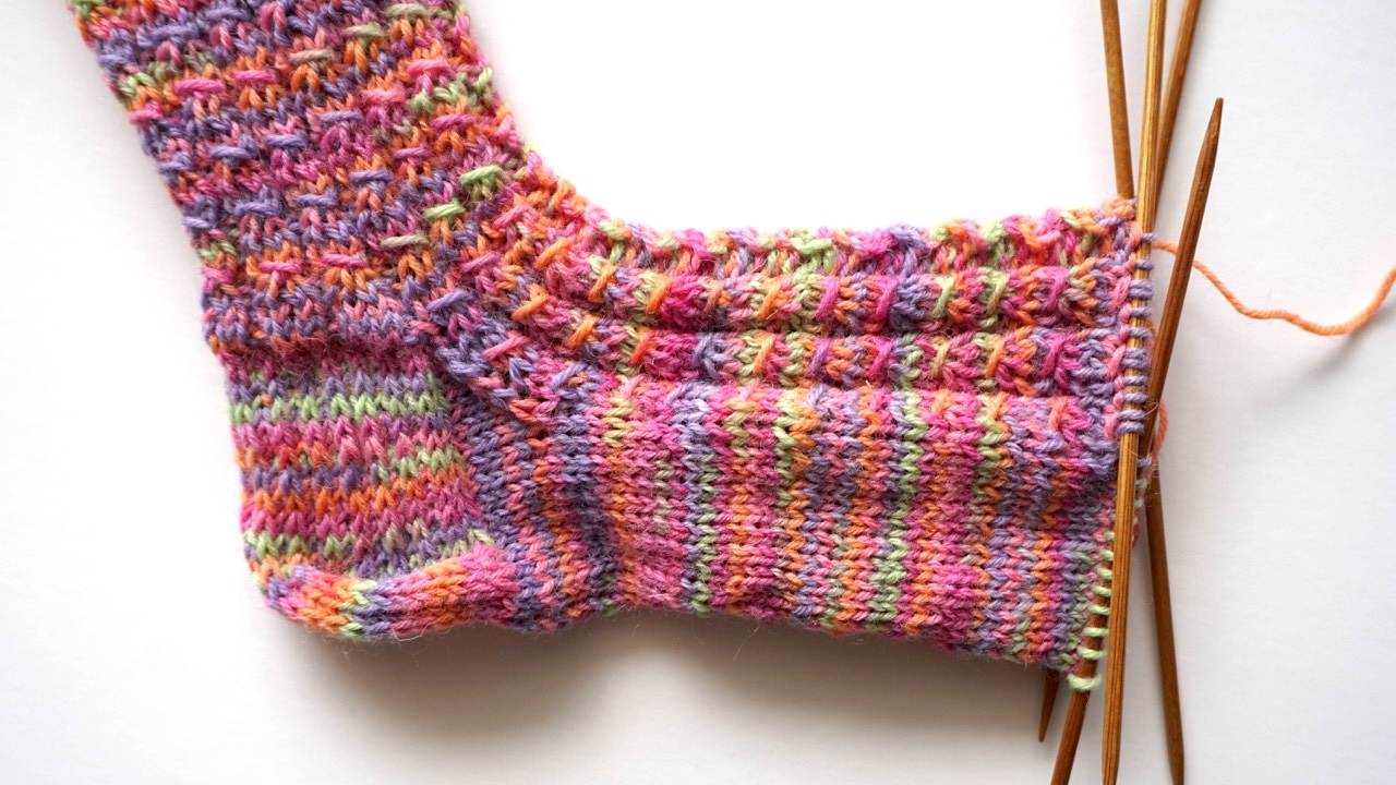 Step-by-step knitting photo showing the faux cable pattern on top of the foot and a smooth sole