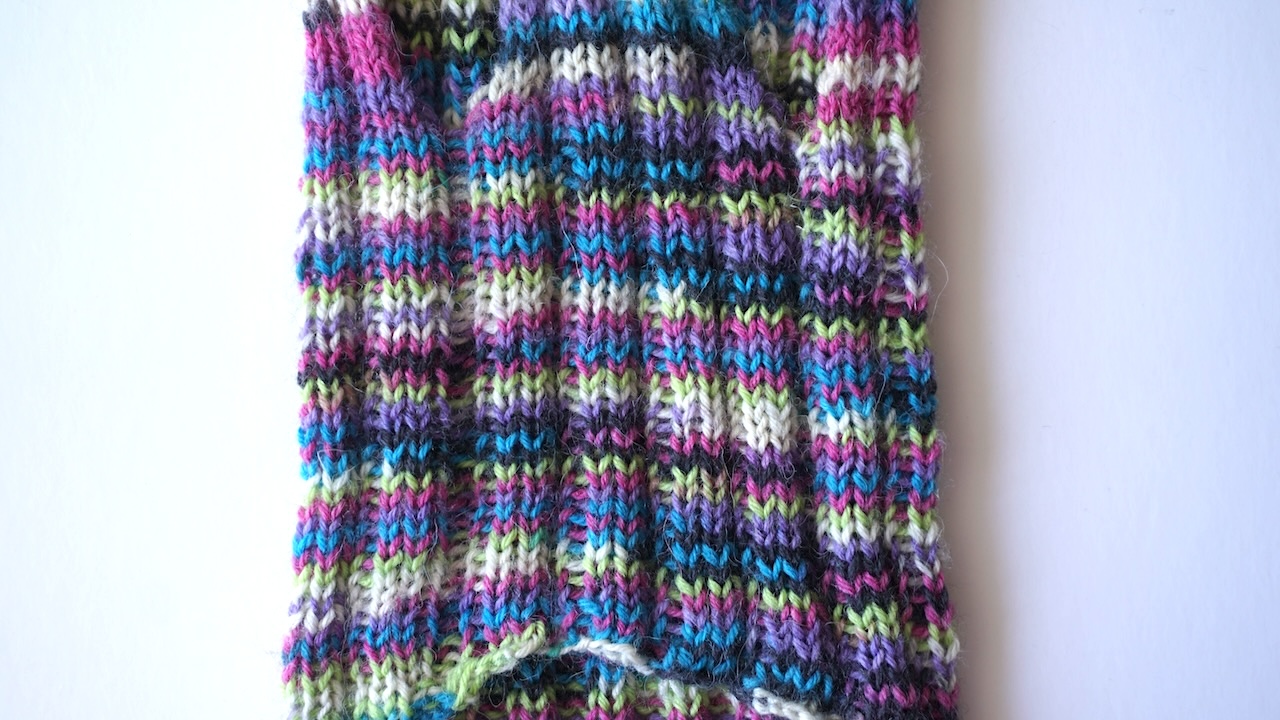 Close-up photo of the lower body of a knitted dog cardigan featuring rib stitches in multicolored yarn