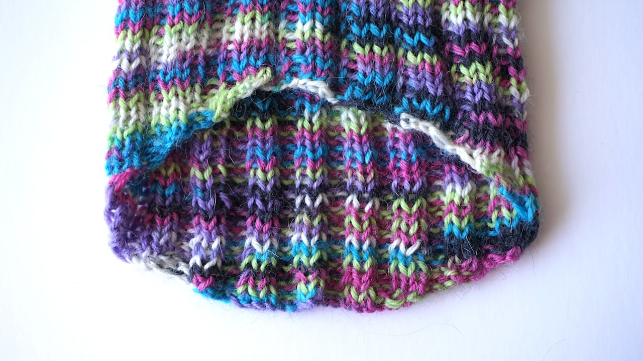 Close-up photo from the belly side of the bind off edge of a knit dog cardigan in multicolored yarn