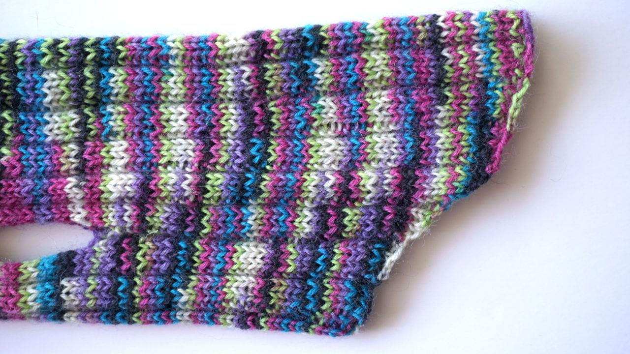 Close-up photo from the side of the bind off edge of a knit dog cardigan in multicolored yarn from the side