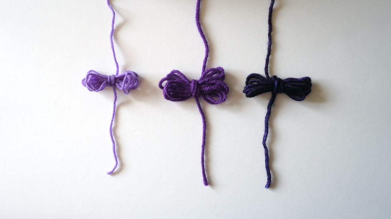Purple yarn wrapped in a bow in three different yarn weights
