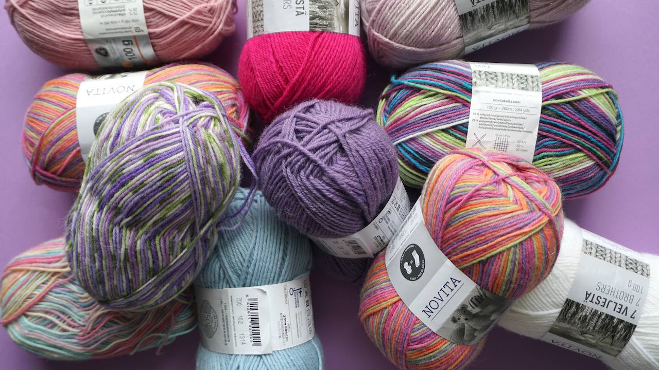 Different colored skeins of wool yarn in a pile with some of them showing a label with the yarn weight chart