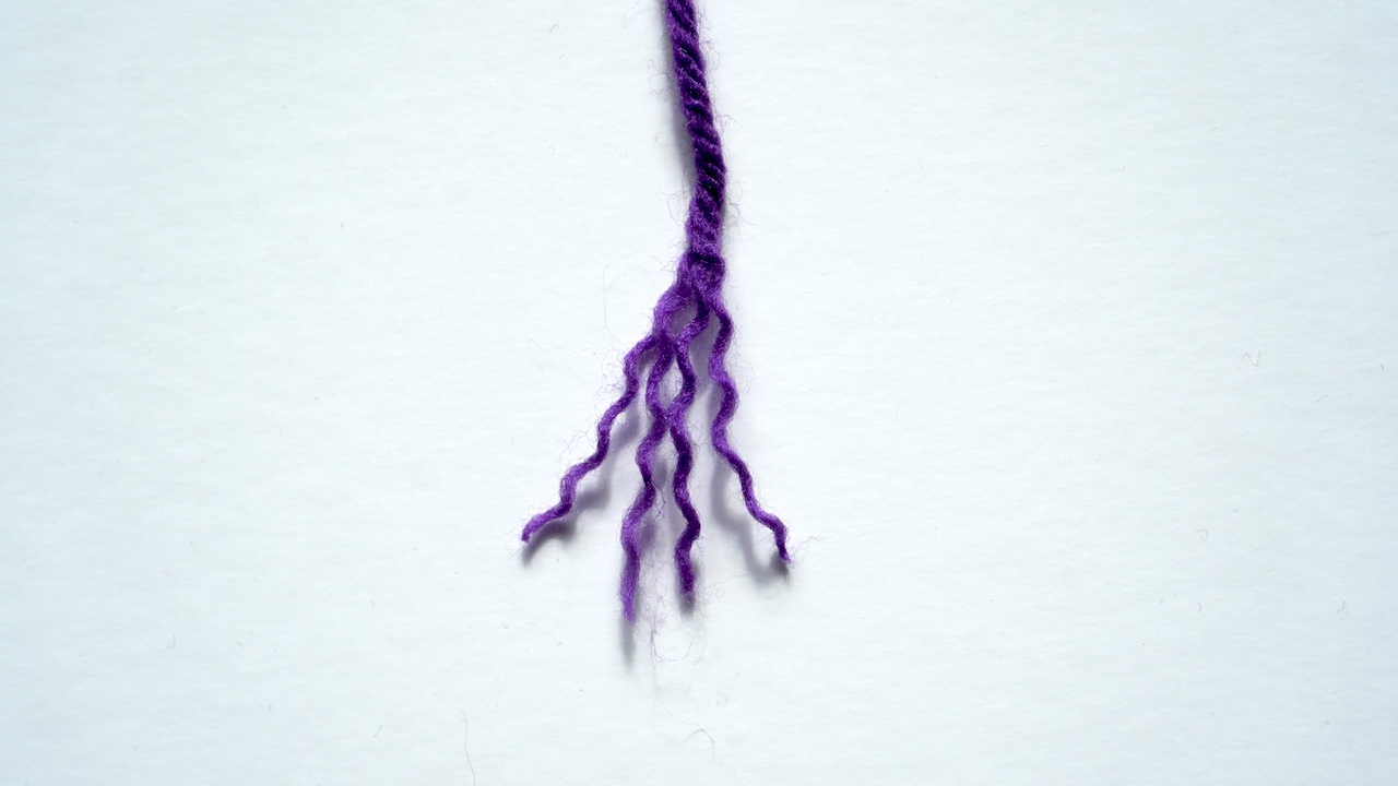 A strand of purple yarn unraveled to show its four plies