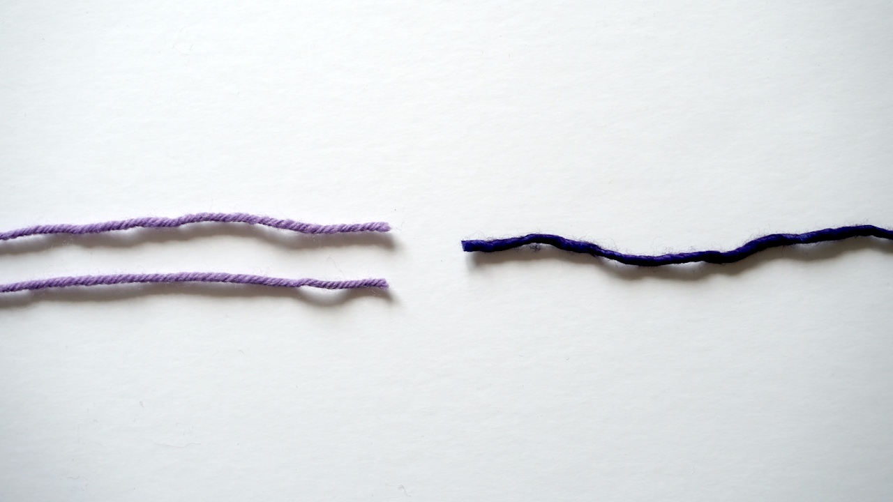 Two strands of fine yarn in lavender color next to one strand of thick yarn in purple color